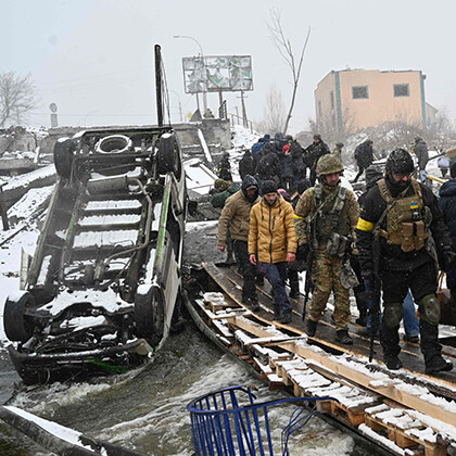 Soldados ucranianos e civis atravessam uma ponte destruída.